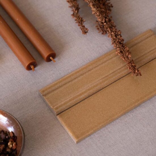 Porcelain stoneware surface in sand color with glossy reflections, accompanied by brown candles and dry twigs on a beige fabric.