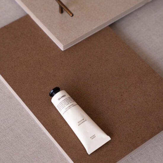 Surface in neutral tones with a light texture, on which rests a tube of cream and a decorative metal element.