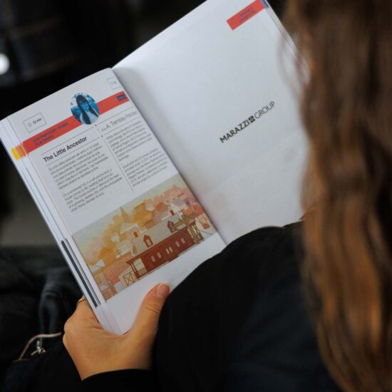 Una persona tiene in mano un libro aperto con illustrazioni e testo, con la scritta "MARAZZI GROUP" visibile.